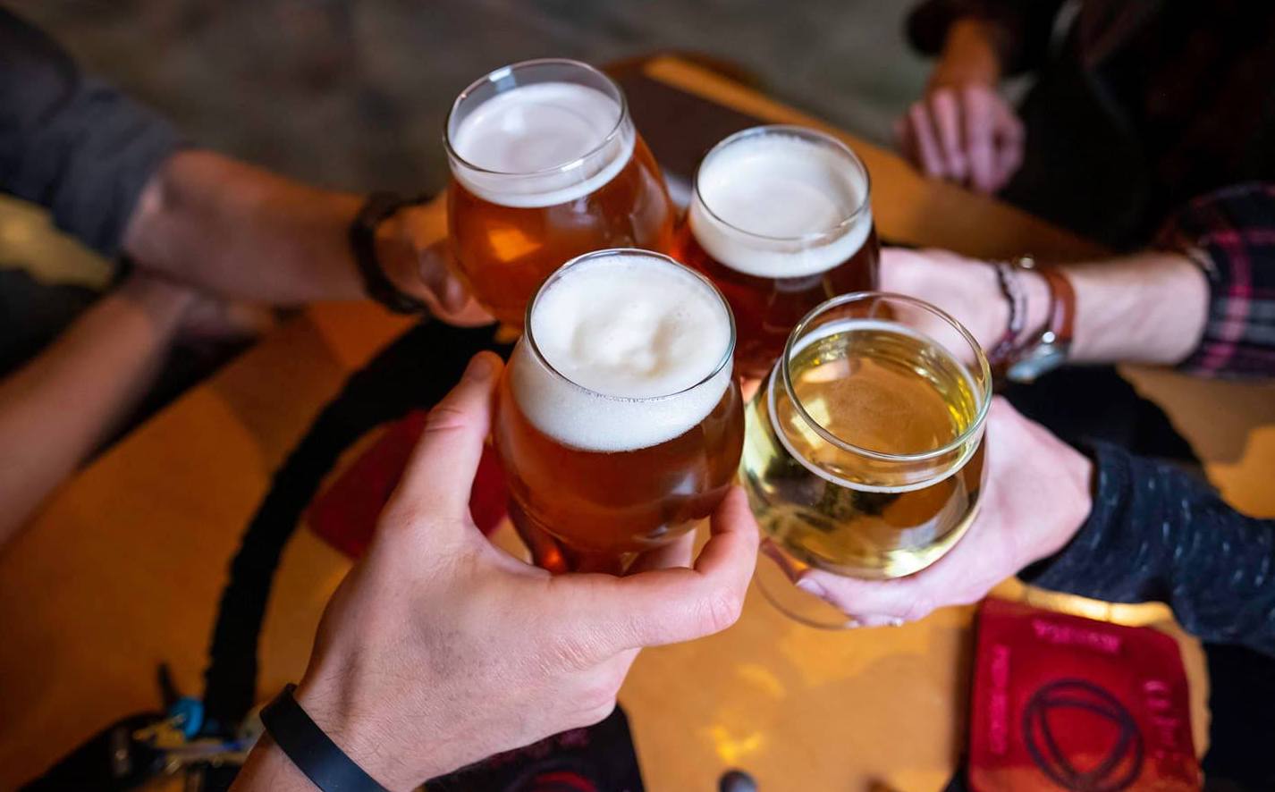 Four hands holding beer glasses cheers together.